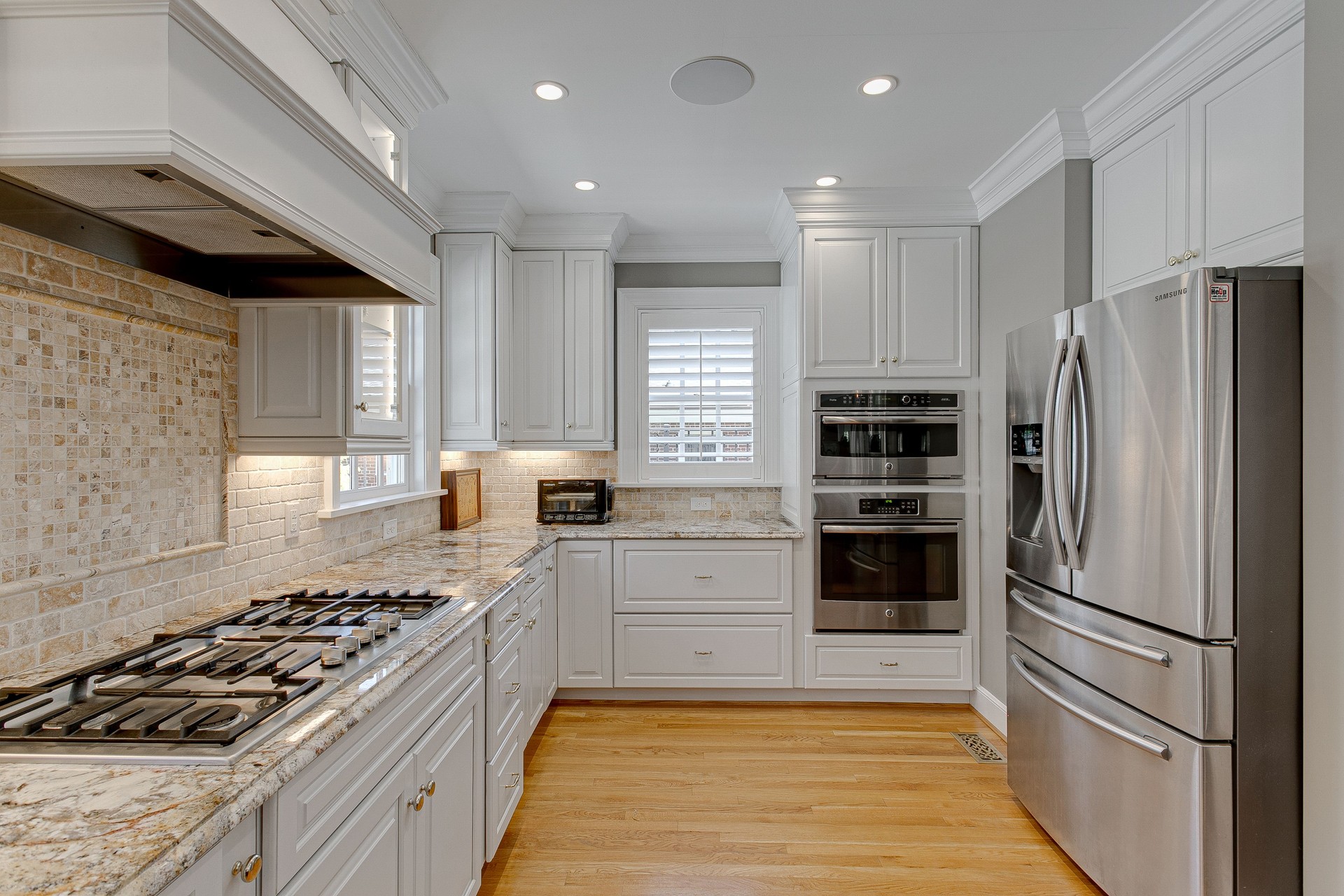Modern Clean Luxury White Kitchen with Stovetop with Backsplash and Stainless Steel Appliances with Hardwood Floors and Plantation Shutters